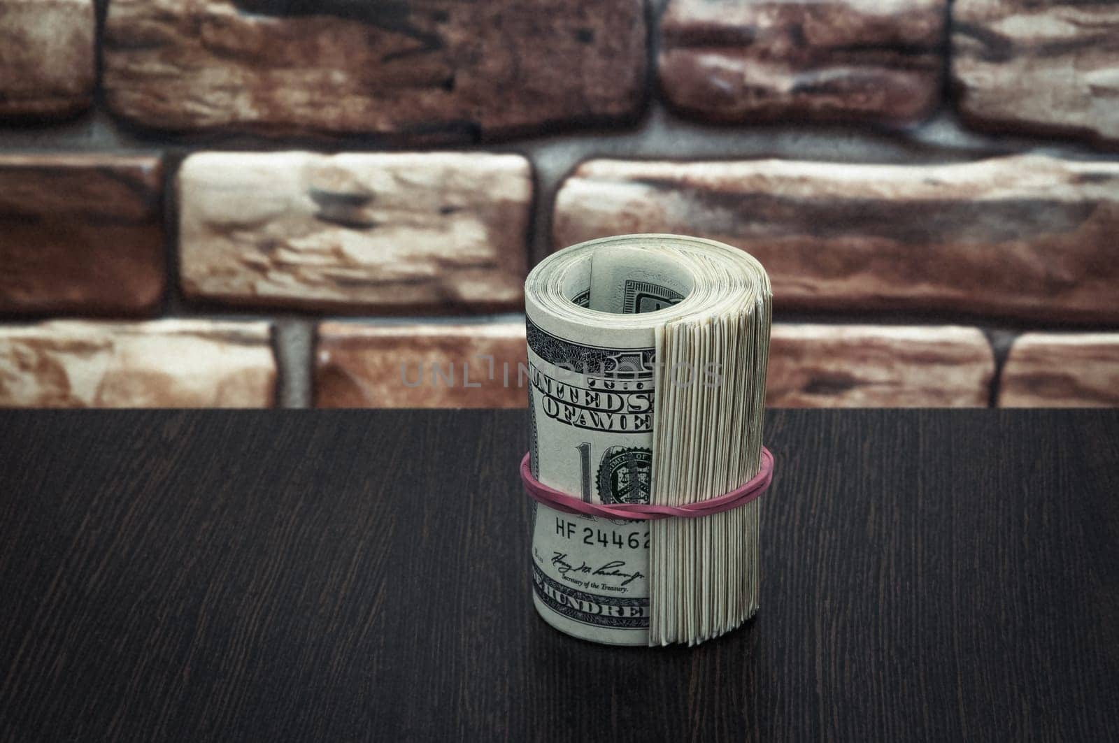 a bundle of American dollar bills of one hundred dollars on a wooden table near a brick wall.