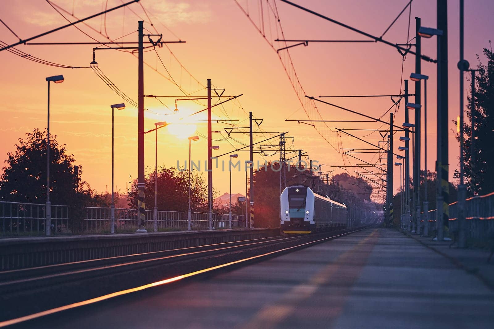 Passenger train commuting to railroad station at colorful sunrise.