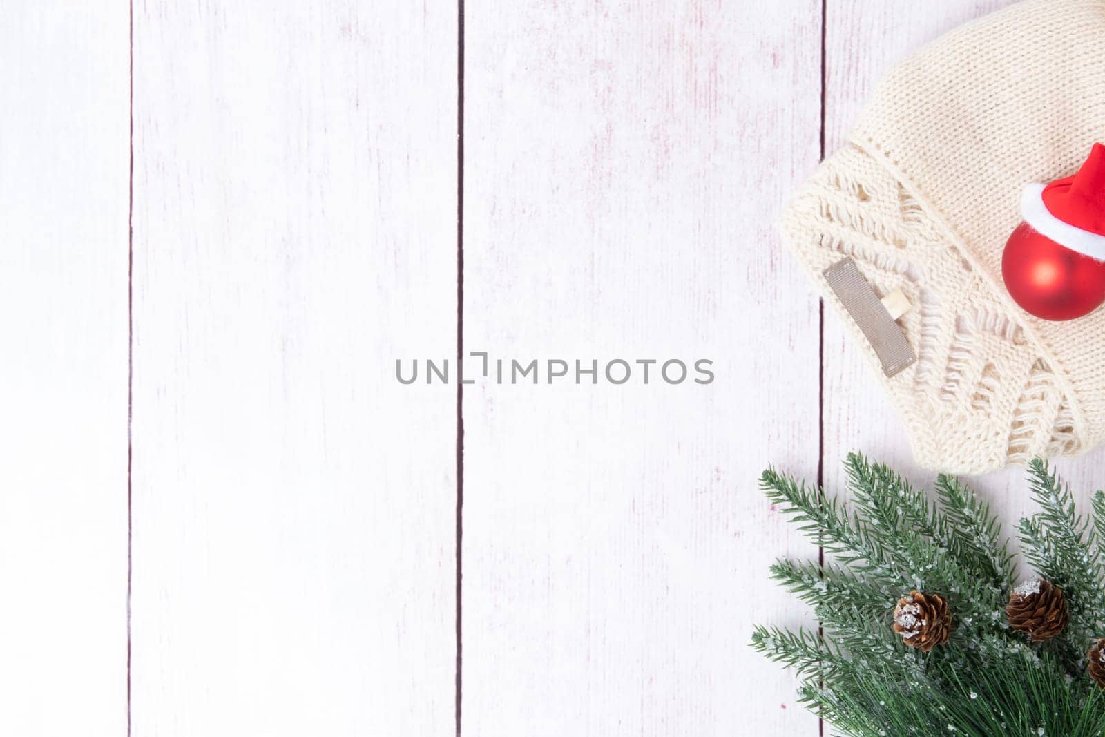 Christmas or winter decoration background. Compostion from christmas tree branches and a winter sweater on a wooden table. Space for design on left site. Top view.