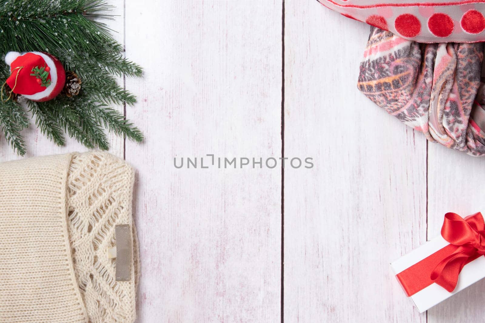 Christmas or winter decoration background. Compostion from christmas tree branches, winter sweater, scarf and a xmas gift box on a wooden table. Space for design. Top view.