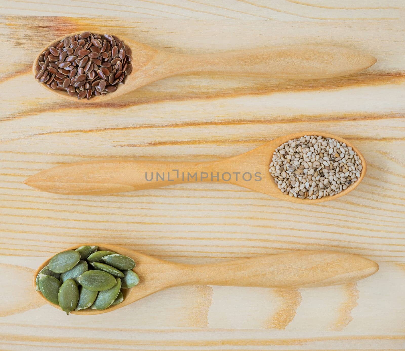Dry ingredient seeds of brown flax, white sesame and pumpkin in wooden spoon, top view on wooden table. Healthy food concept