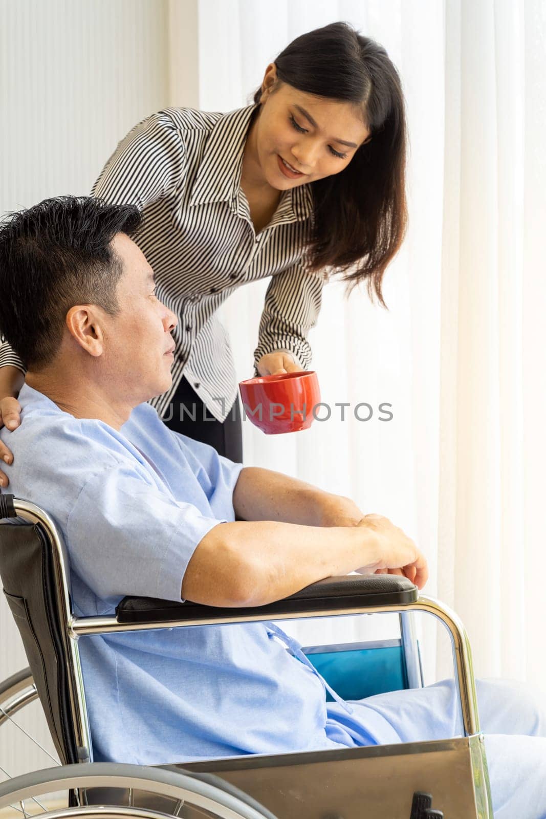Elderly patient with red cup coffee and his relative on wheelchair is looking through the window