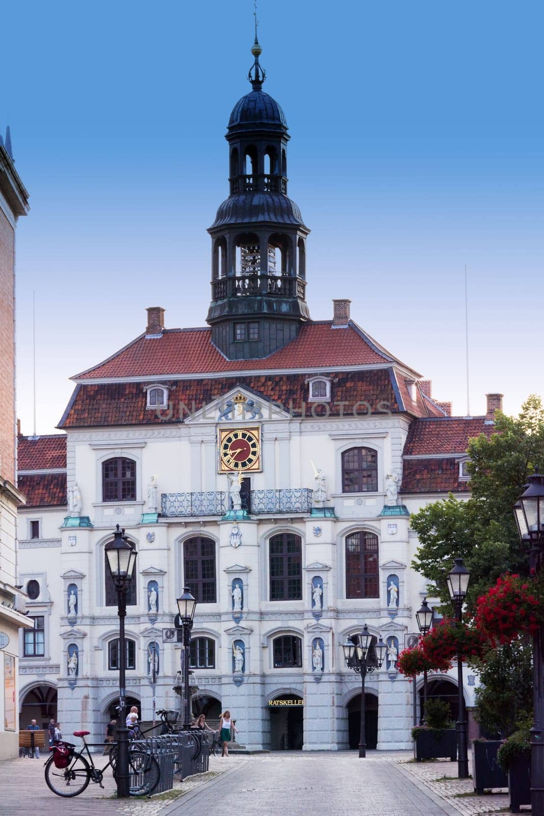 LÜNEBURG, NIEDERSACHSEN, GERMANY - JULI 27, 2018:.Vintage Straßenlaterne Laterne mit Blumenbeet. Historisches Rathaus im Hintergrund in Lueneburg Deutschland...Lueneburg, Lower Saxony, Germany - July 27, 2018:.Vintage street lamp lantern with flowerbed. Historic city hall in the background in Lueneburg Germany.