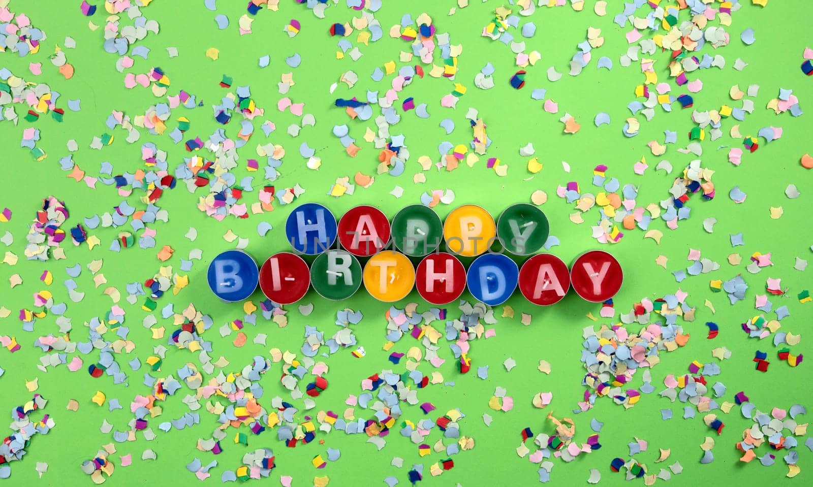 Colorful birthday candles with confetti on green cardboard