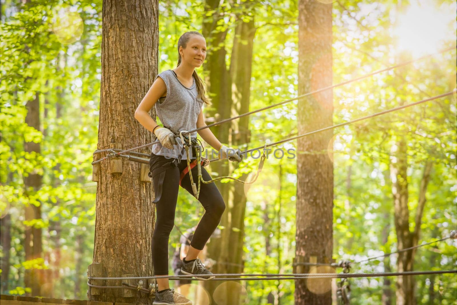 young, blond girl climbs in summer in climbing forest / high ropes course