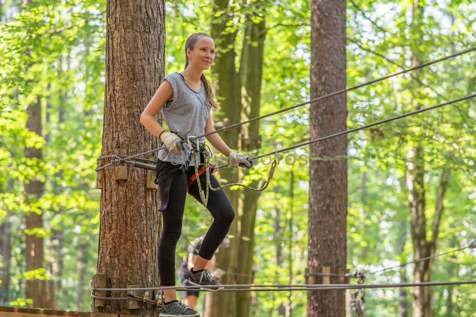 young, blond girl climbs in summer in climbing forest / high ropes course