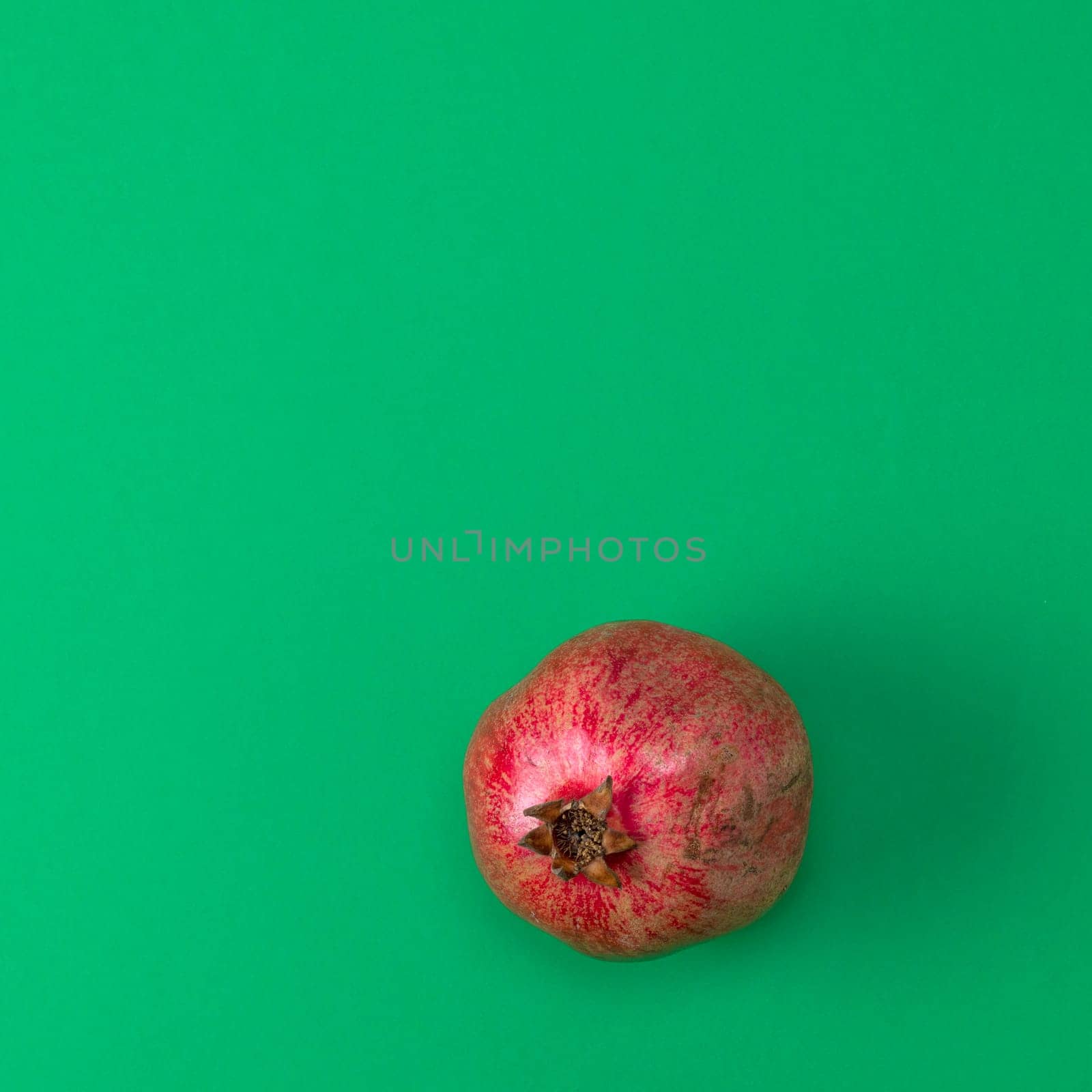 red pomegranate in the peel on a green background, copy space