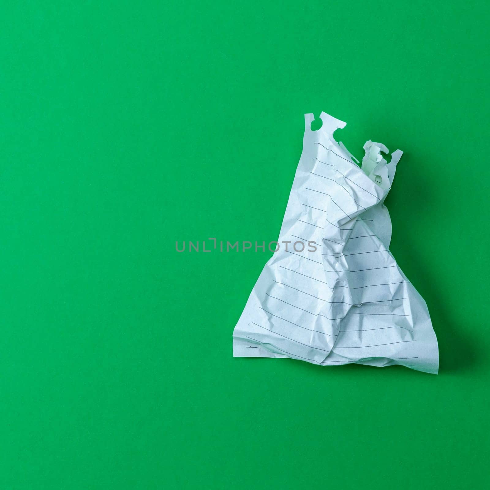 wrinkled white sheet torn from a notepad on a green background, empty space on the left
