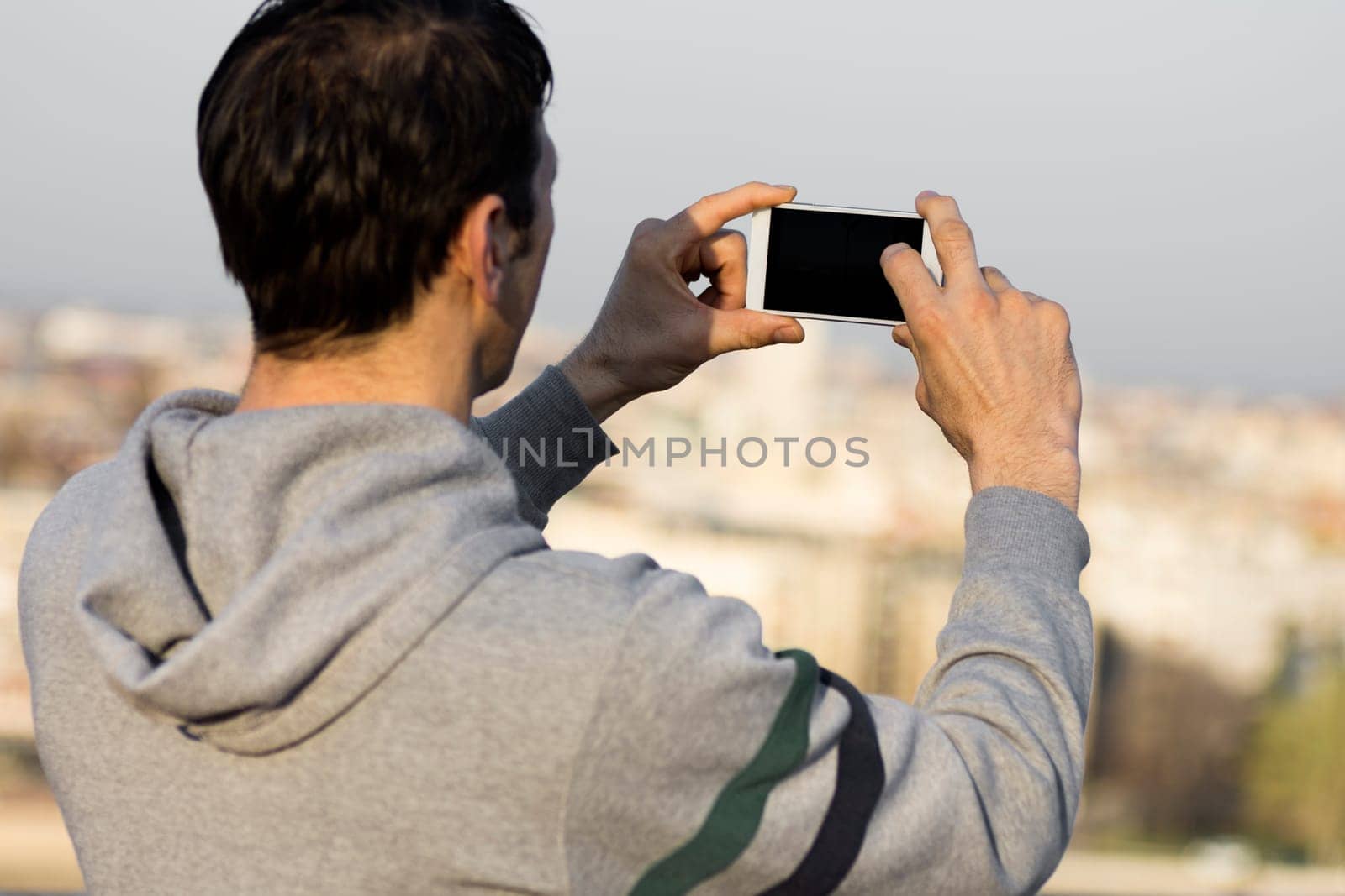 The tourist is using mobile phone for taking a picture about city.
