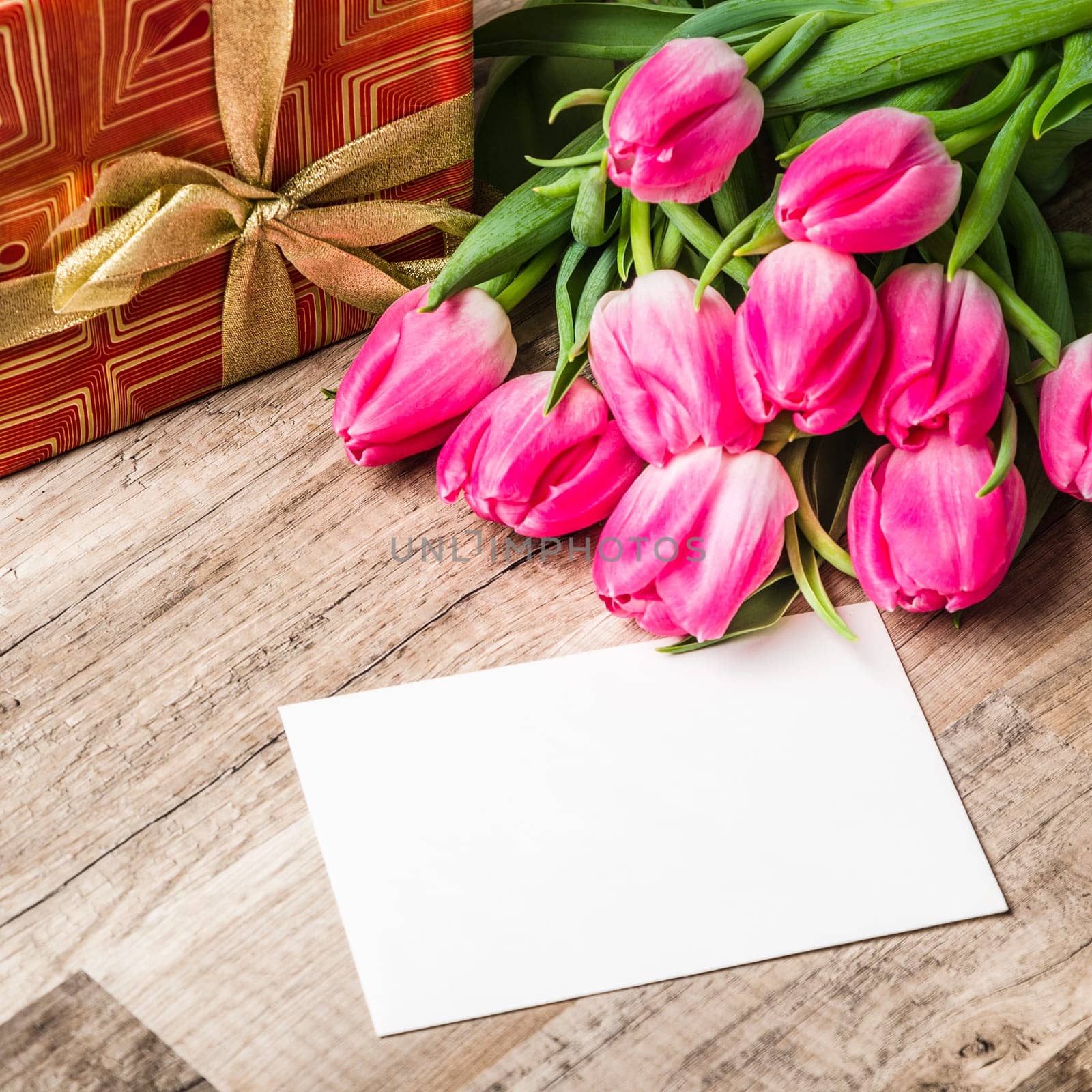 Beautiful bouquet from pink tulips and a gift on a table