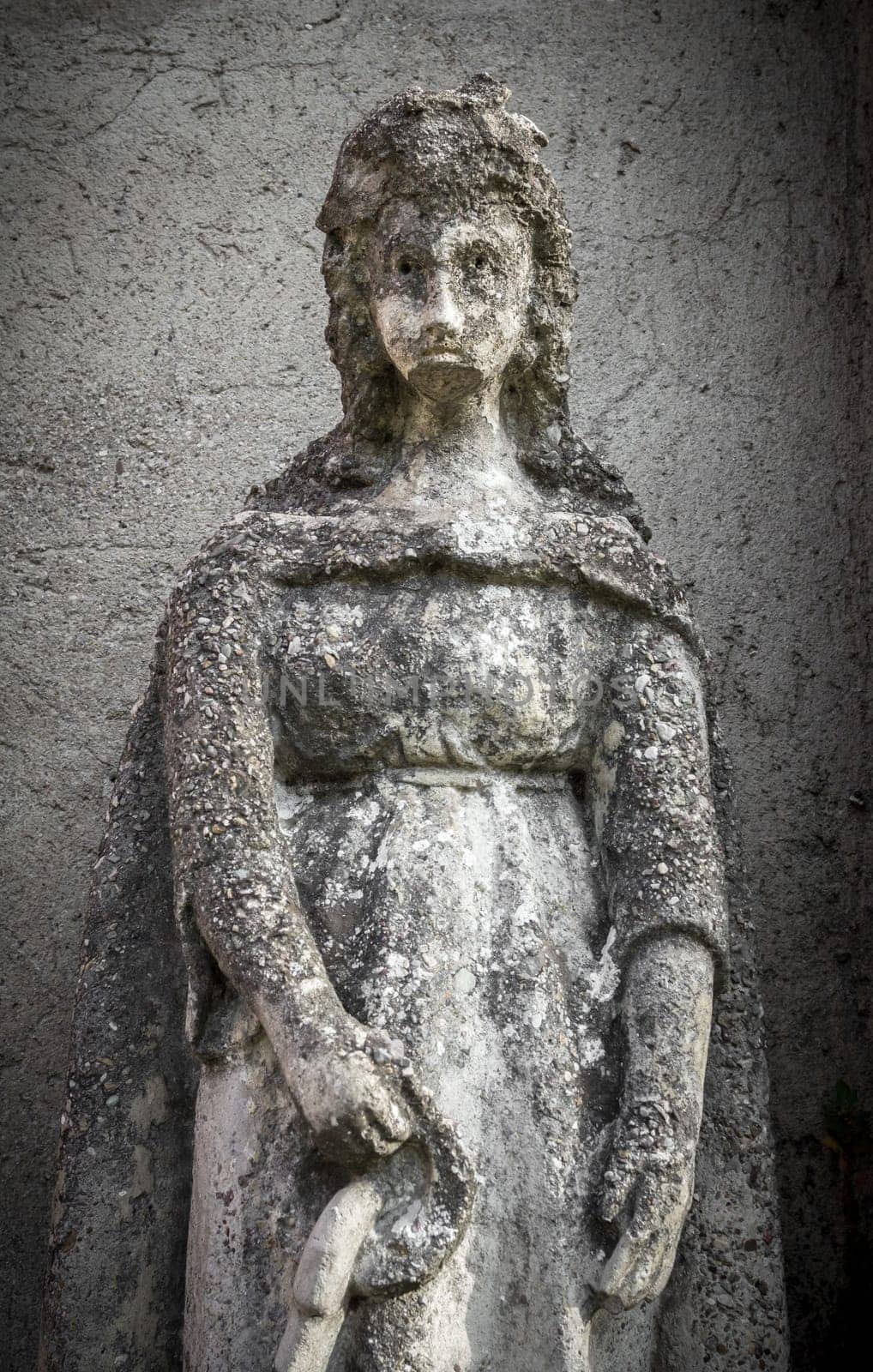 Statue of a beautiful woman with a sad expression. On background a gray and rough wall. Ideal for concepts and backgrounds.