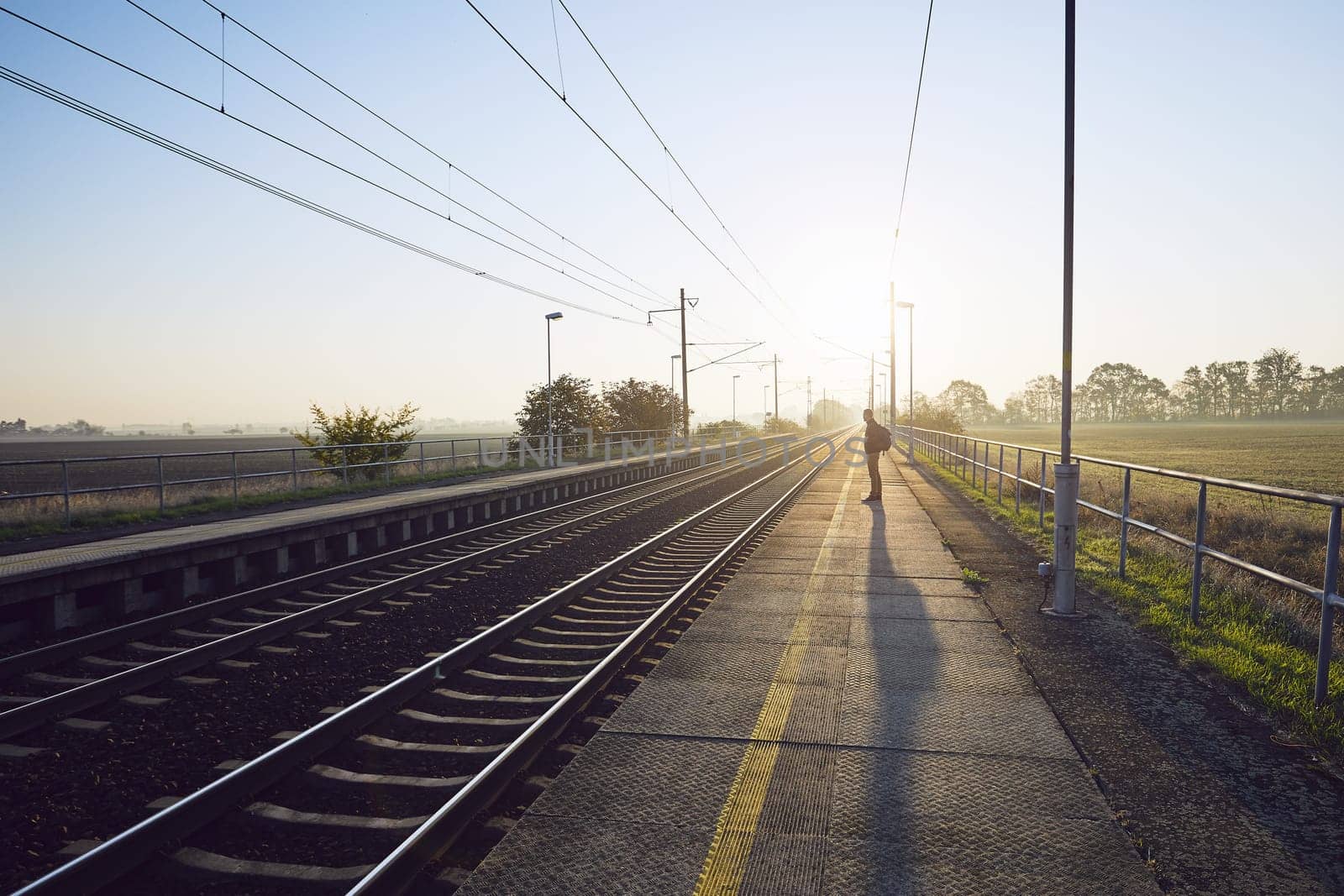Alone young man with backpack waiting for train at railroad station at sunrise.