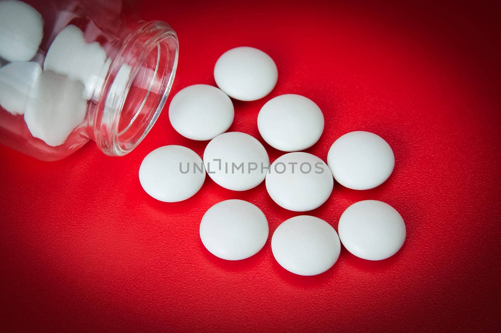 White tablets are scattered from a glass bottle on a red background. Vignetting