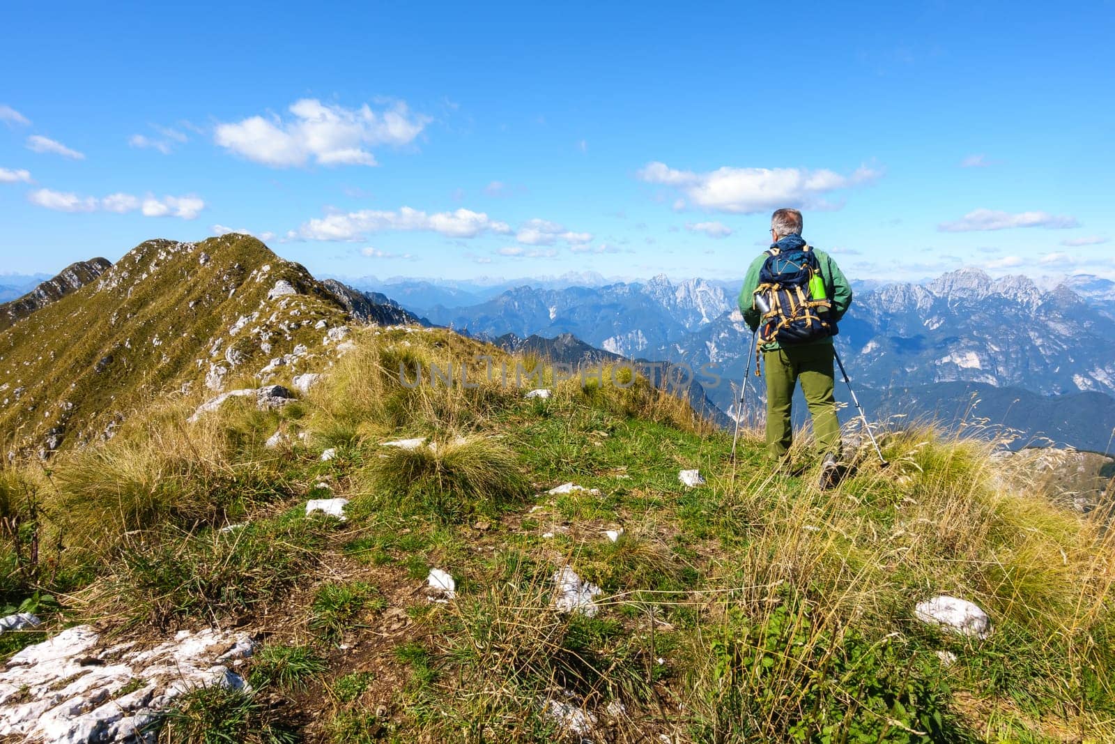 Man hiker walking on top of mountain against blue sky.