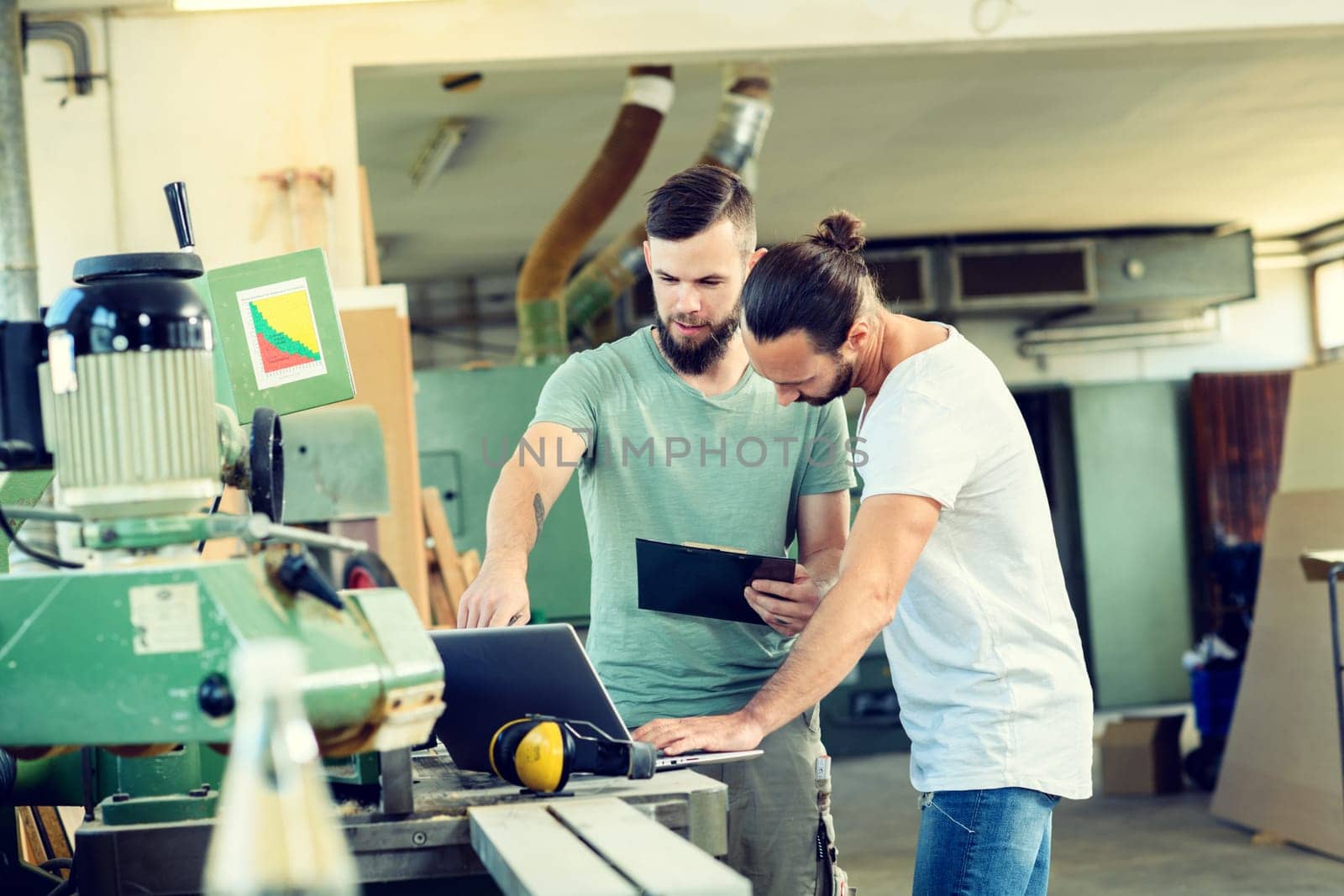 two worker in a carpenter's workshop with clipboard and computer