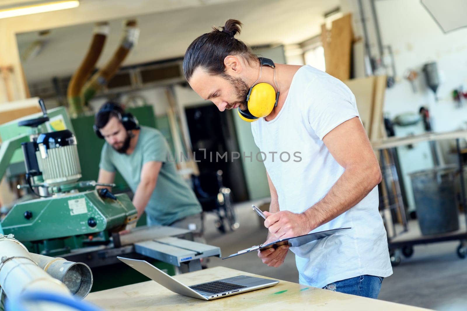 worker in a carpenter's workshop with clipboard and computer