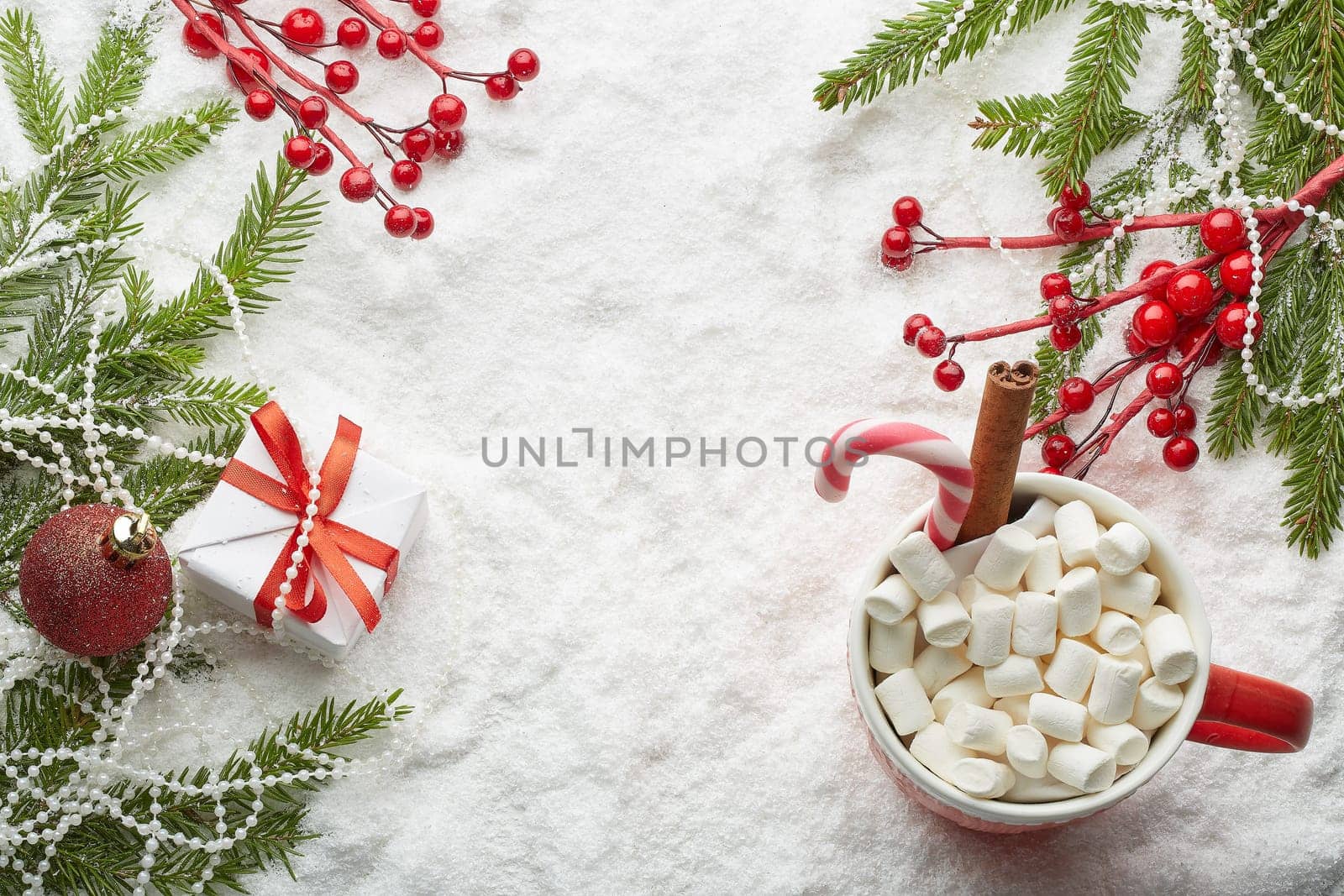 Fir tree branches with decorations, gift and mug with cacao and marshmallow on a snow background with copy space. Top view. Christmas and New Year. Winter holiday