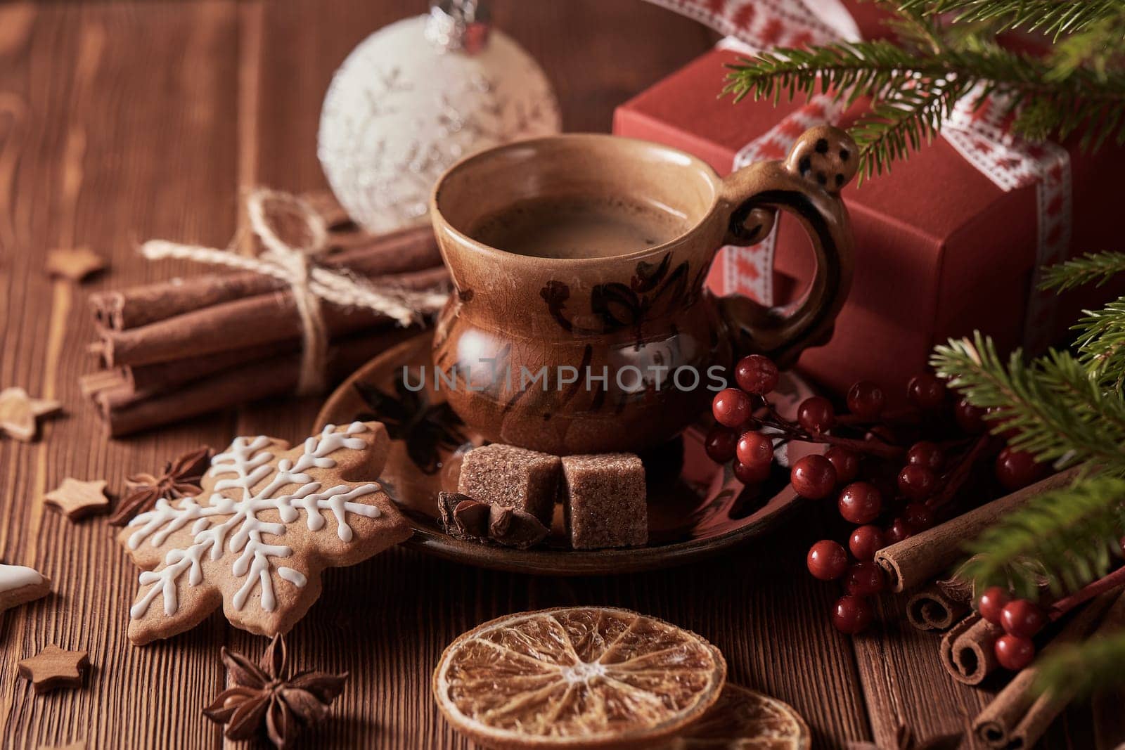 Cup of coffee, gingerbread cookies, gift box, fir tree branches with decorations on a wooden brown background. Christmas and New Year treat.