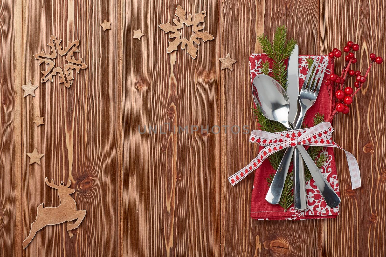 Spoon, knife and fork on red napkin with fir tree branch on a wooden background. Top view with copy space for adding your content. Menu. Advertising
