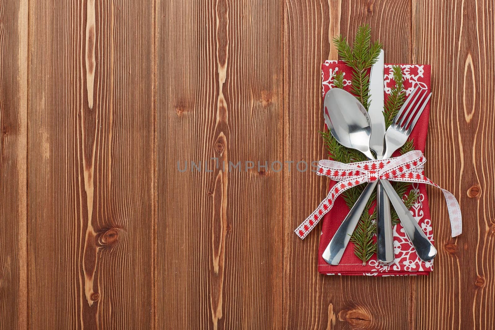 Spoon, knife and fork on red napkin with fir tree branch on a wooden background. Top view with copy space for adding your content. Menu. Advertising