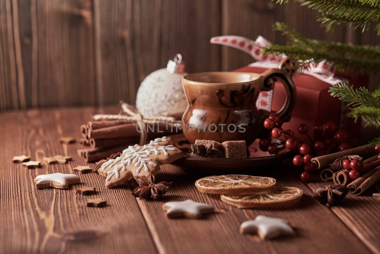 Cup of coffee, gingerbread cookies, gift box, fir tree branches with decorations on a wooden brown background. Christmas and New Year treat.