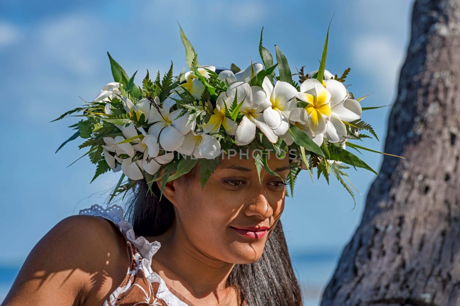 Young woman with flower wreath from Frangipani leans against palm trunk,Raiatea,French Polynesia