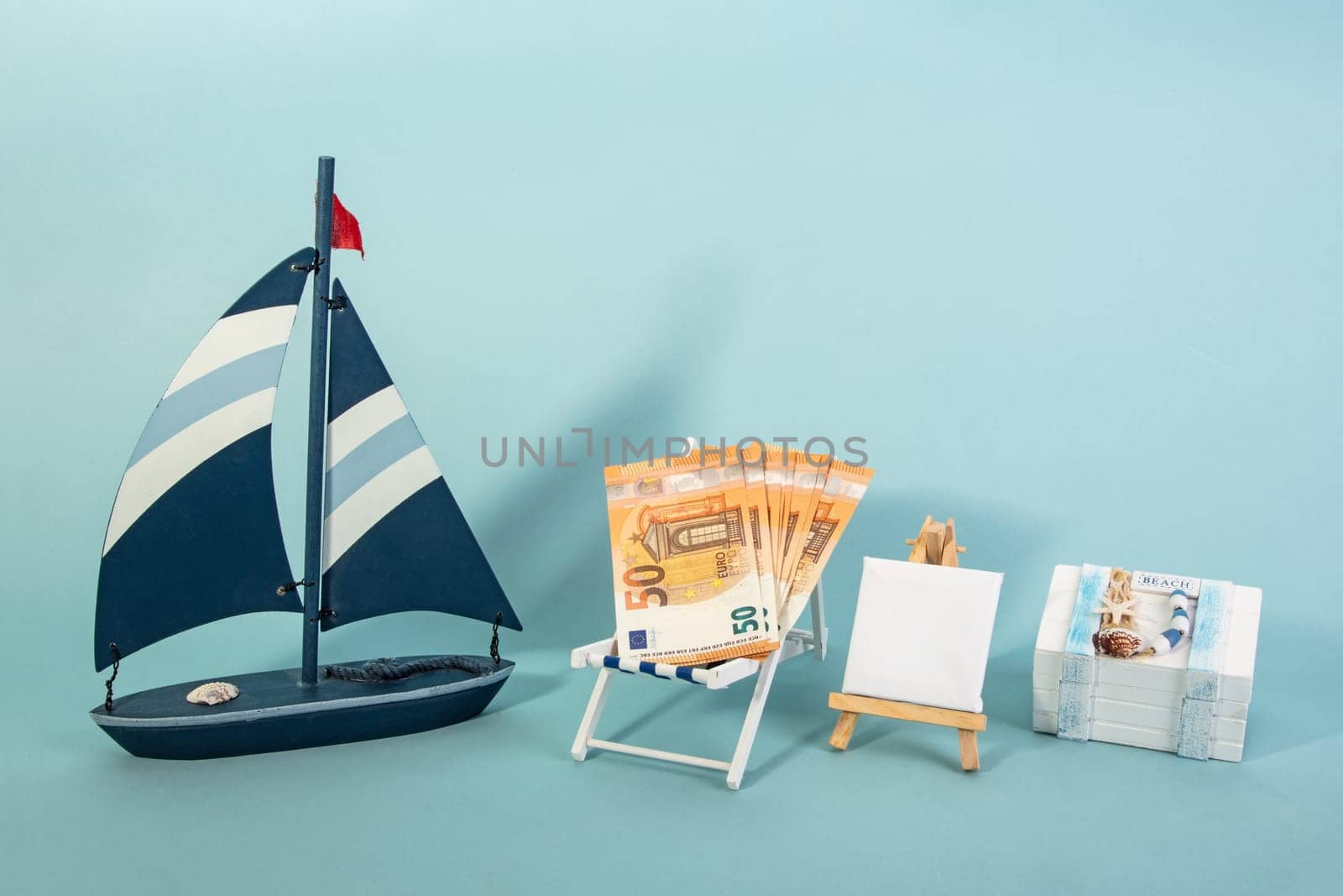 Summer Vacation Concept with toy boat with fifty Euro Banknotes on blue background