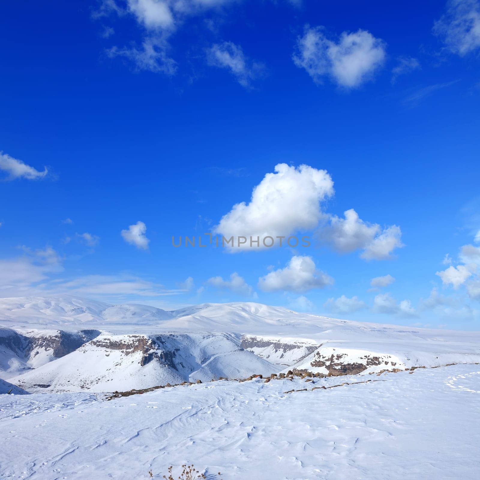 Snow covered empty frozen landscape of mountainside over blue sky with clouds
