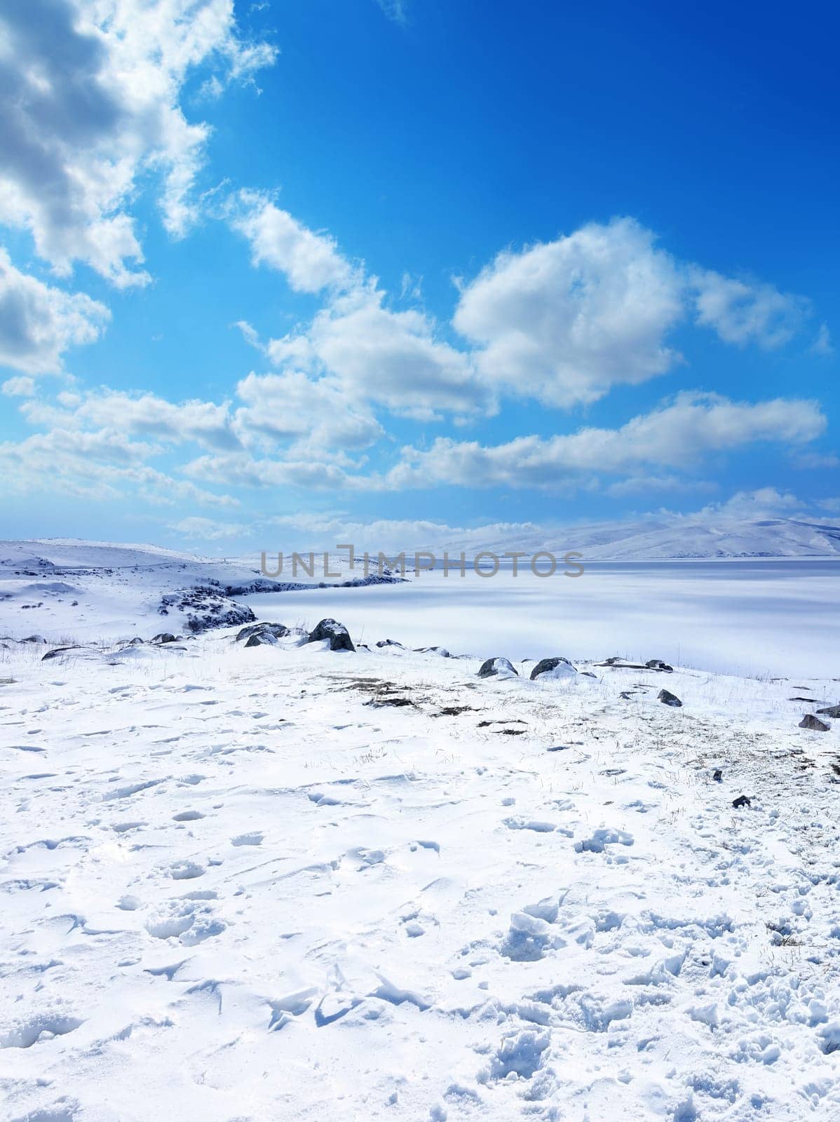 Snow covered empty frozen landscape of mountainside over blue sky with clouds