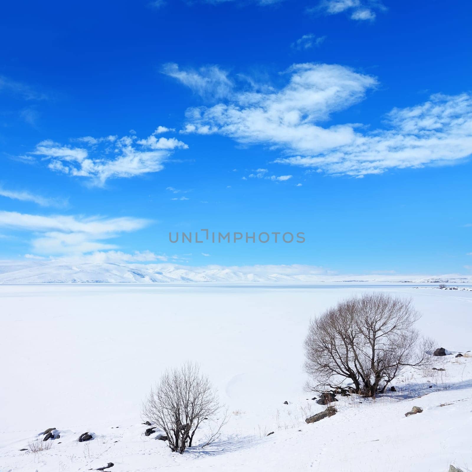 Snow covered empty frozen landscape of mountainside over blue sky with clouds