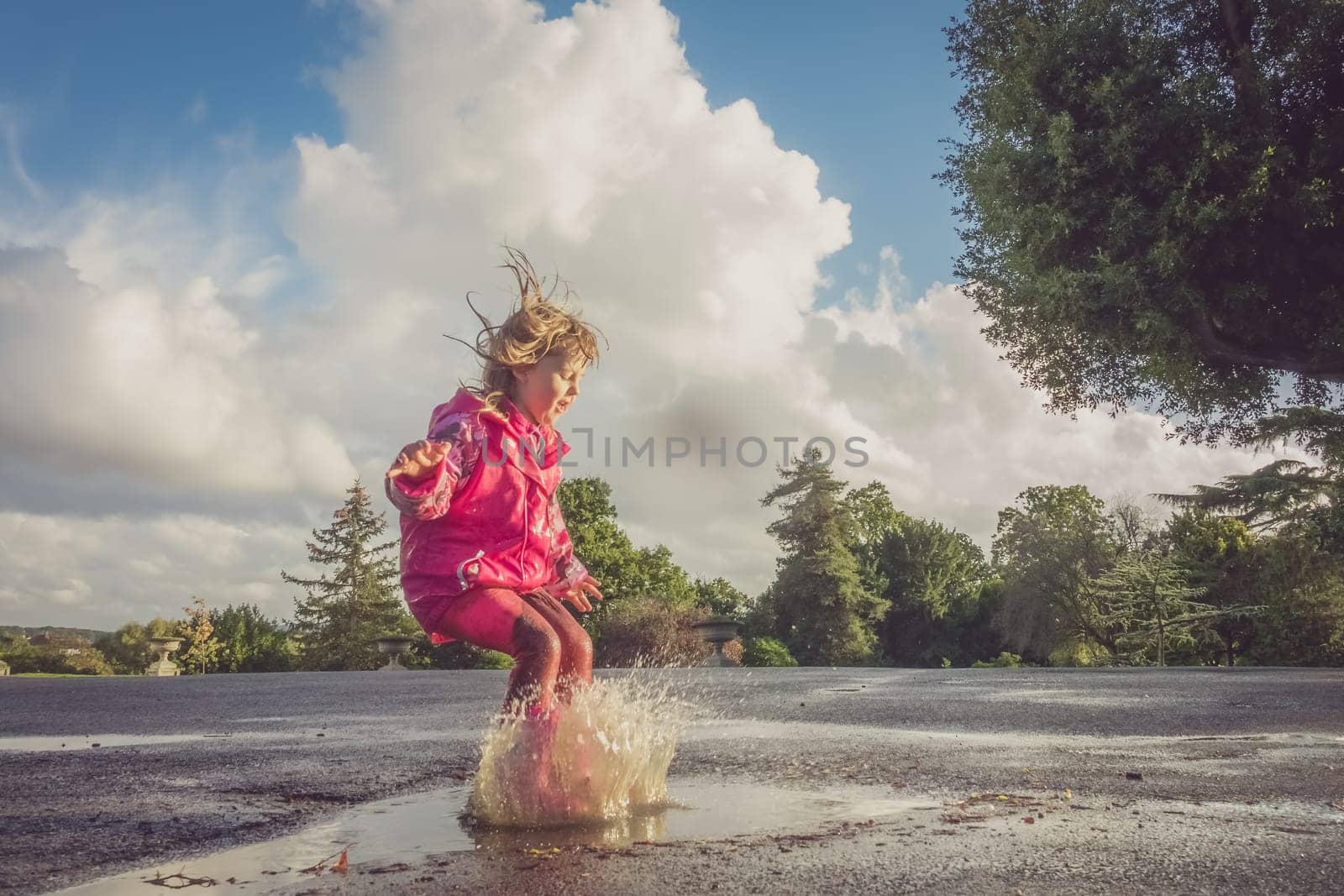 Little Caucasian girl jumping into the puddle after rain in english countryside