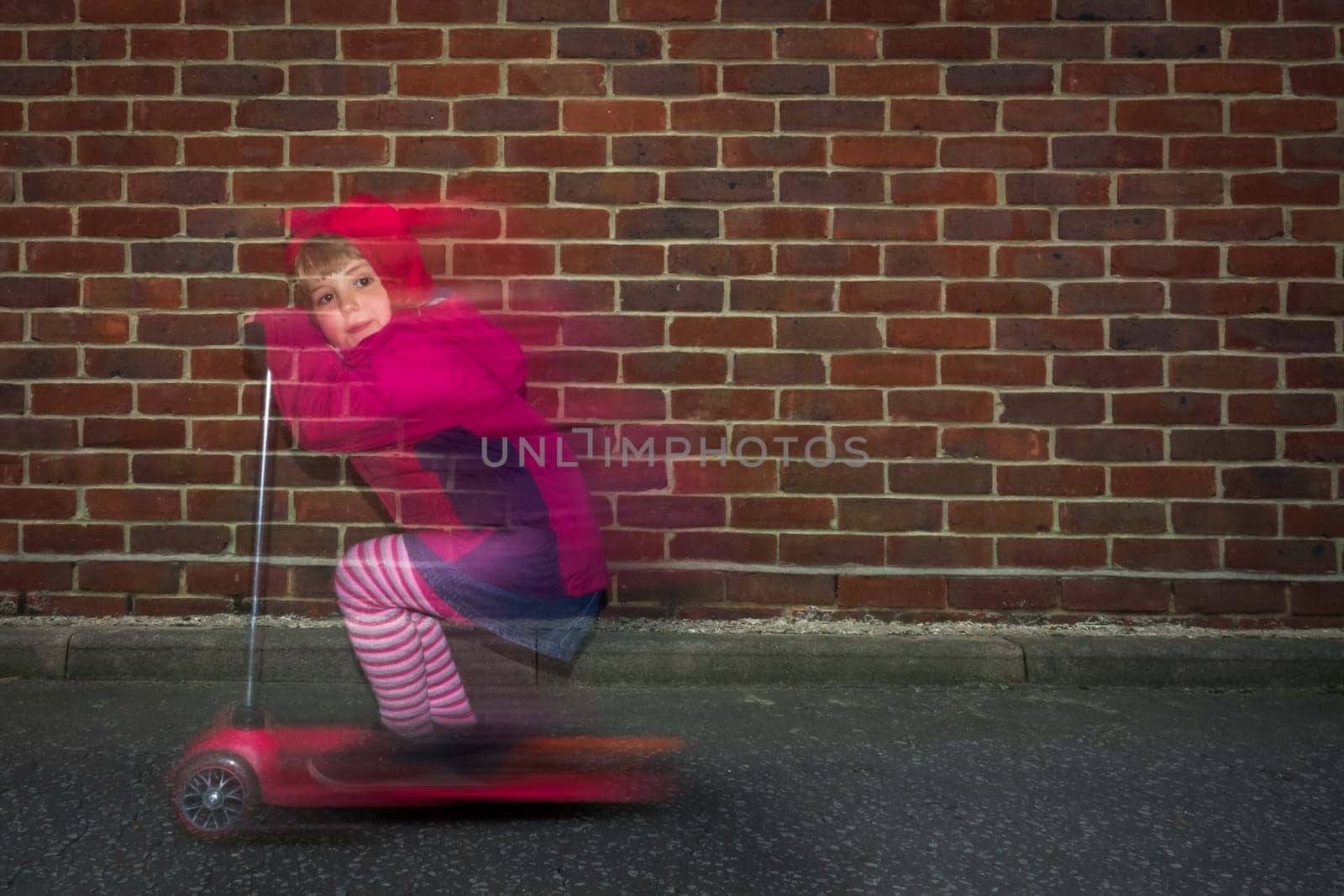 Little Caucasian girl riding fast on her scooter on a road outside her house