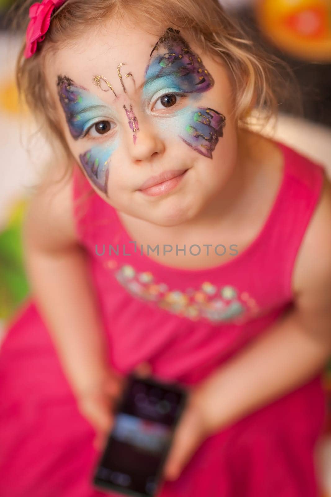 Cute little Caucasian girl having butterfly painted on her face during children birthday party