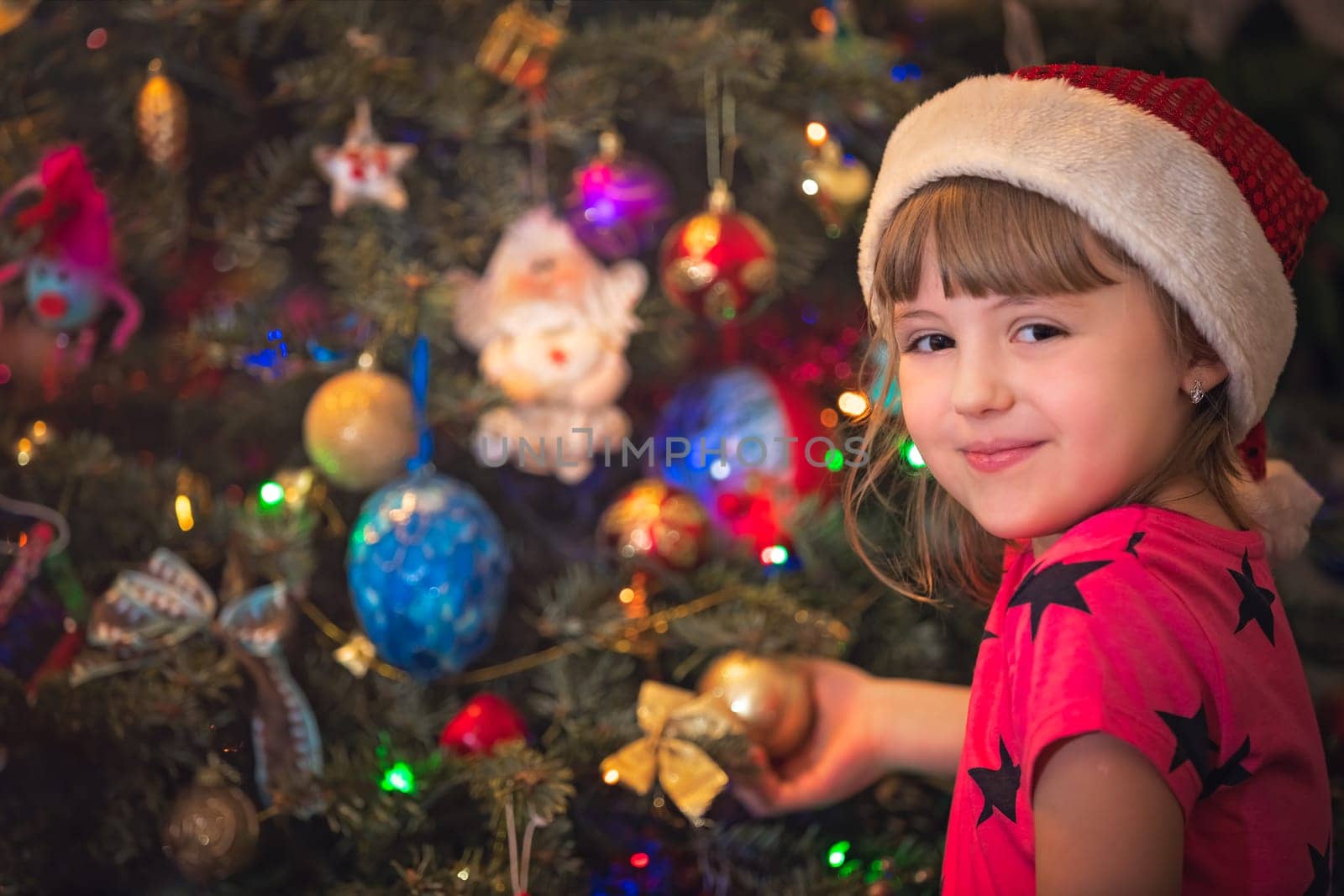 Cute happy and smiling Caucasian Christmas girl putting the decorations on the Christmas tree
