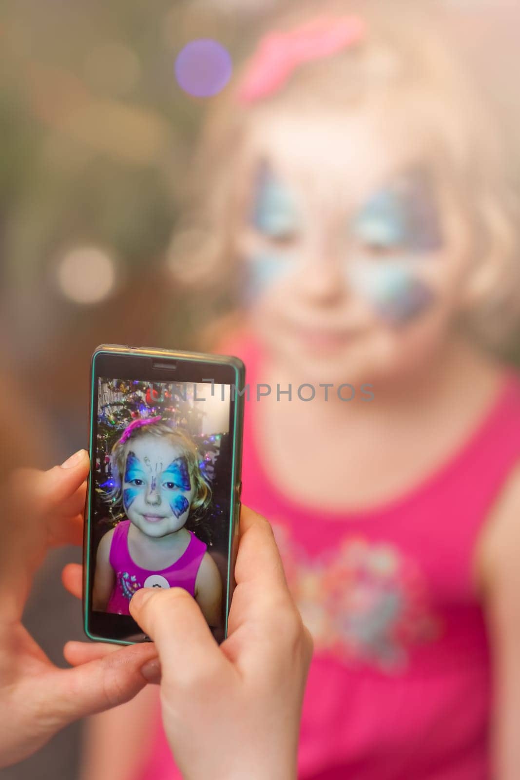 Mother taking picture on a smarphone mobile phone of her little daughter girl having her face painted during party