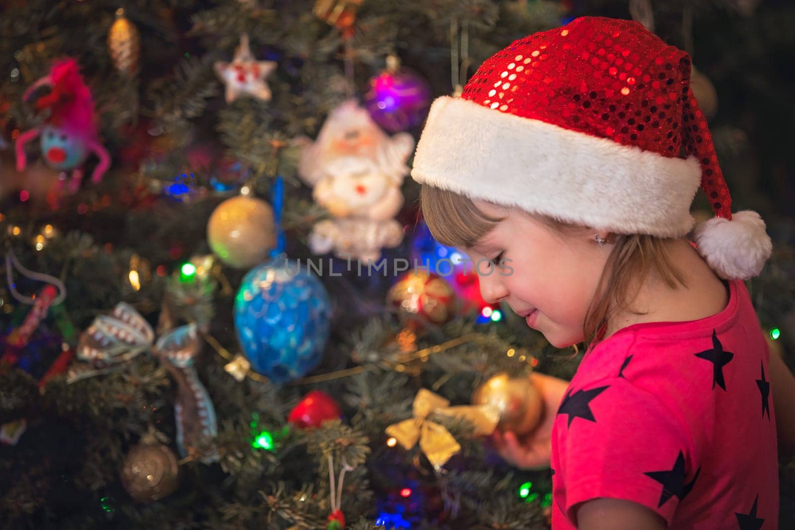 Cute happy and smiling Caucasian Christmas girl putting the decorations on the Christmas tree