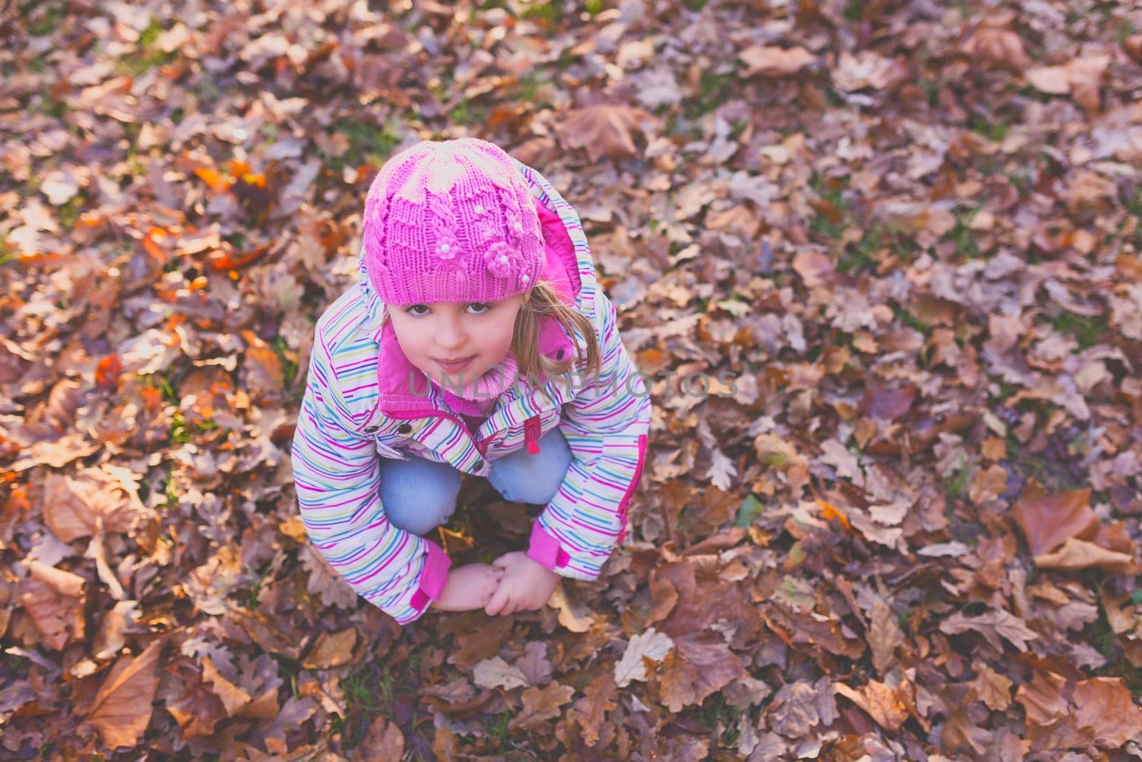 Portrait of a cute girl wearing pink hat resting on the ground full of autumn leaves
