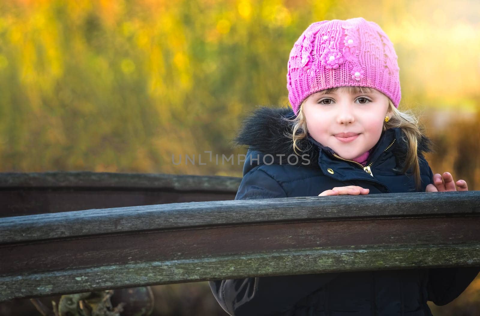 Romantic portrait of a cute little caucasian girl standing on a small wooden bridge in a park, with warm background bokeh