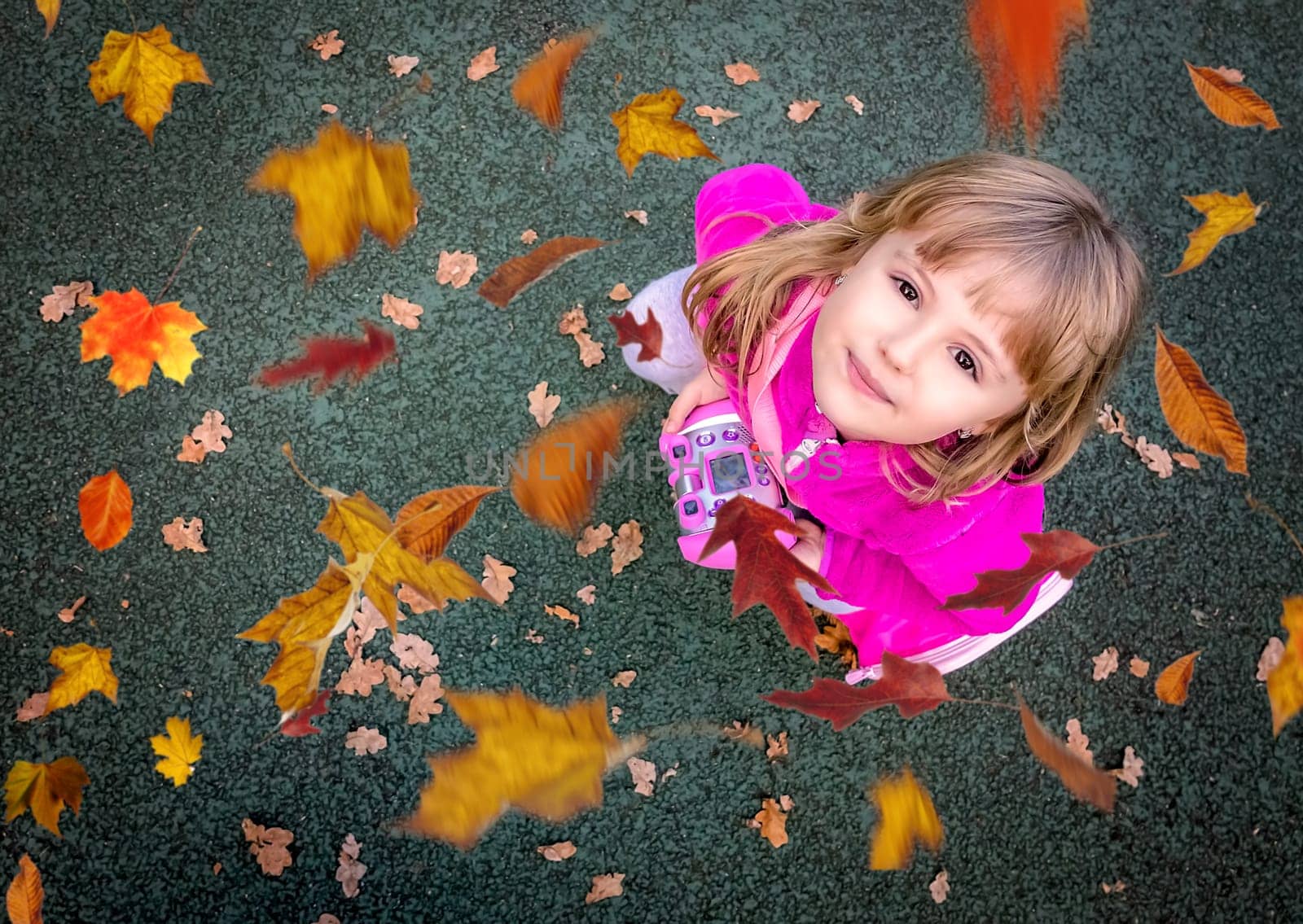 Portrait of a cute little Caucasian girl with looking up at the falling leaves in autumn