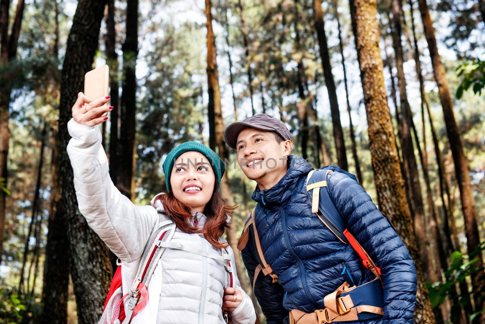 Attractive asian hikers couple taking selfie photo with mobile phone on the forest