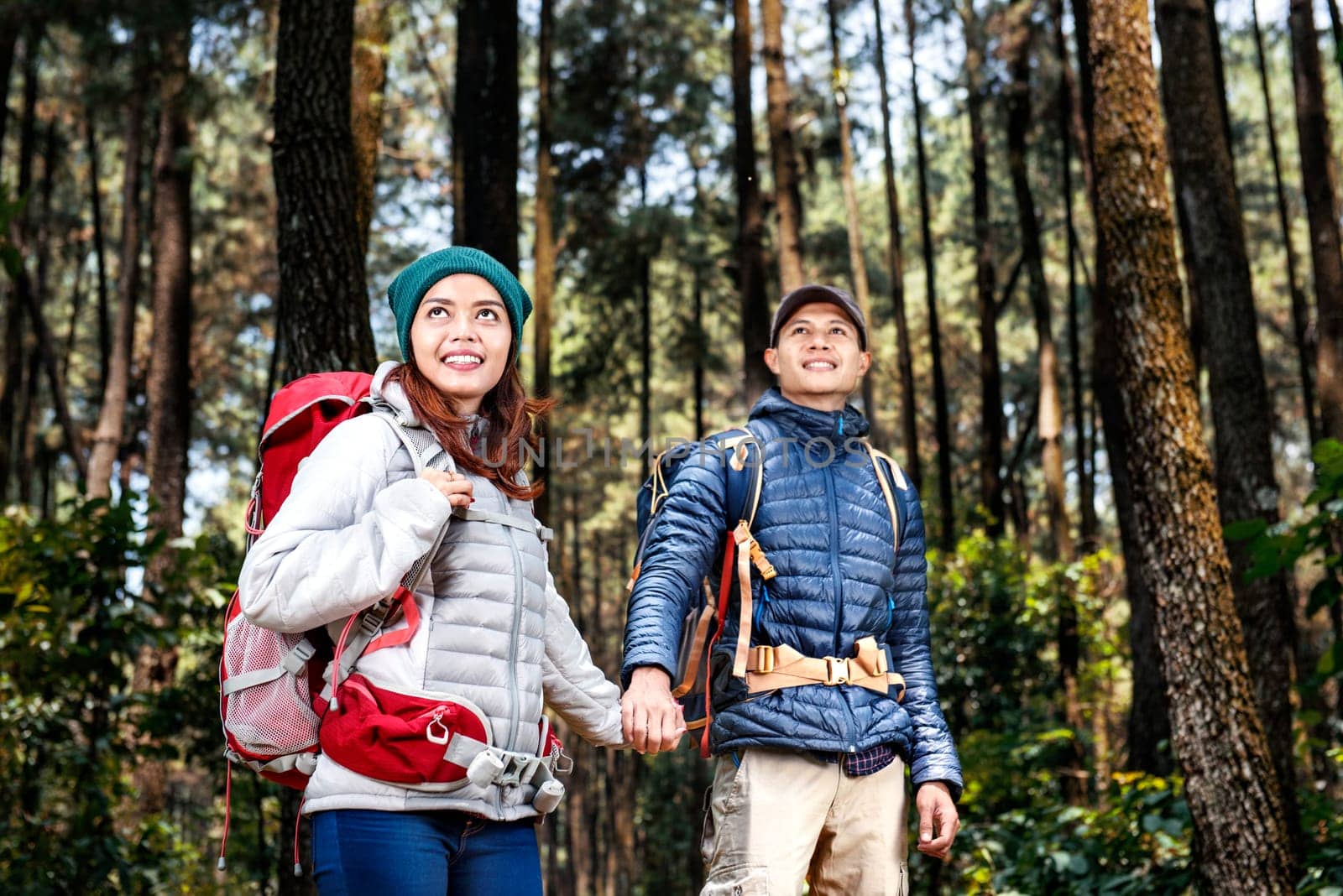 Happy asian hikers couple with backpack walking while holding hands on the forest