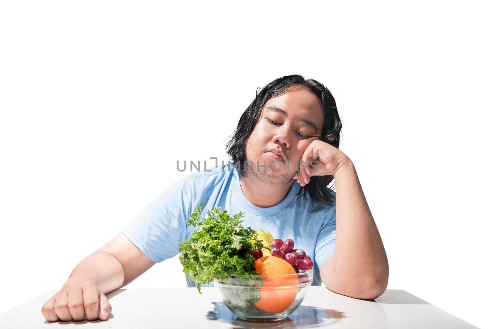 Asian fat man sad looking at healthy food (fruit and vegetables) on the desk isolated over white background. Fat man diet concept.