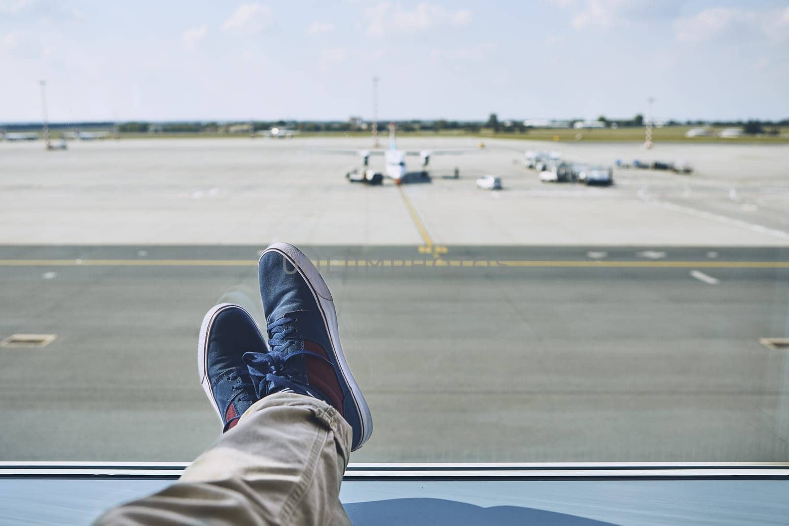 Man waiting at airport. Personal perspective of traveler from window to taxiways and runway.