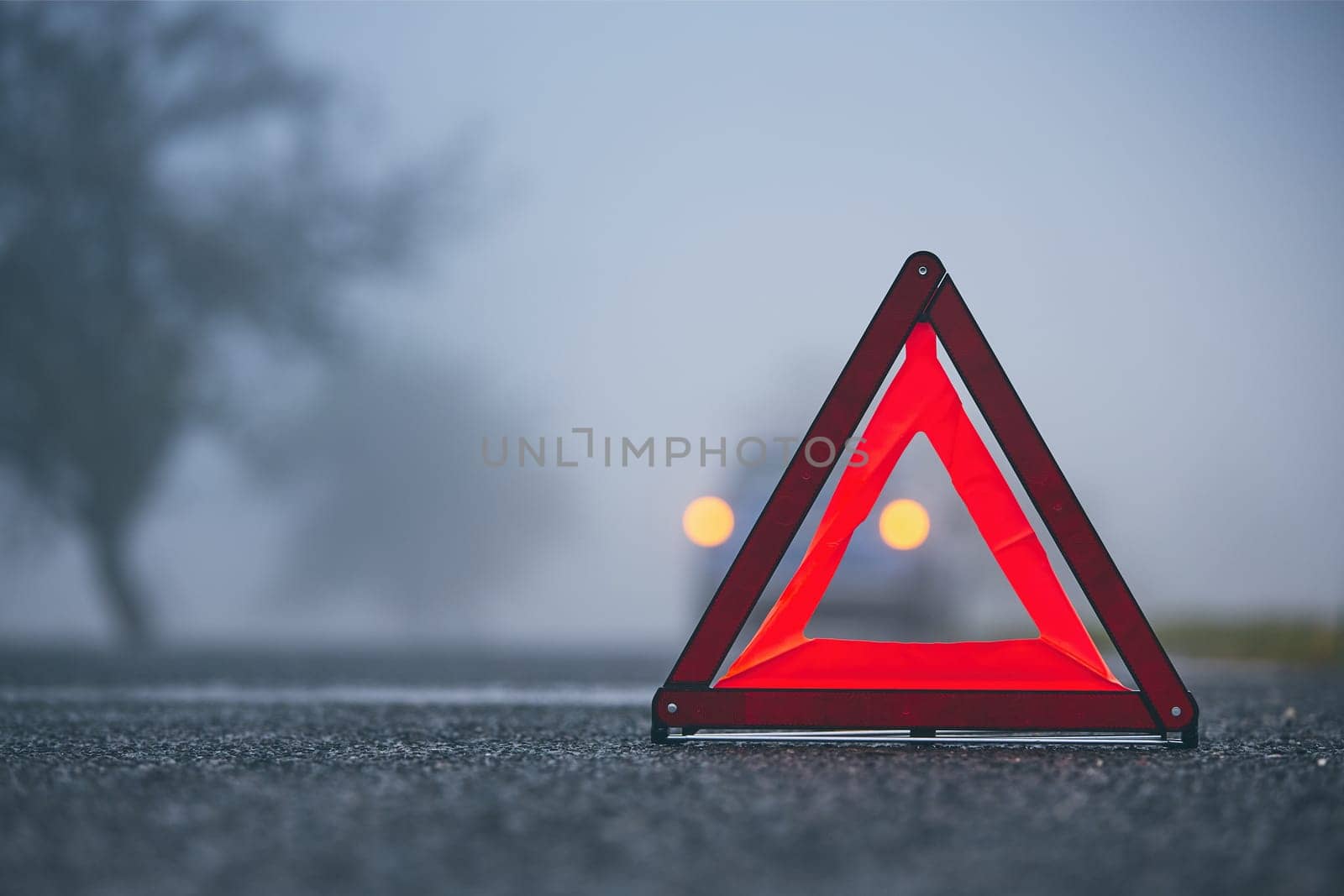 Traffic problem in thick fog. Car on the road behind warning triangle.