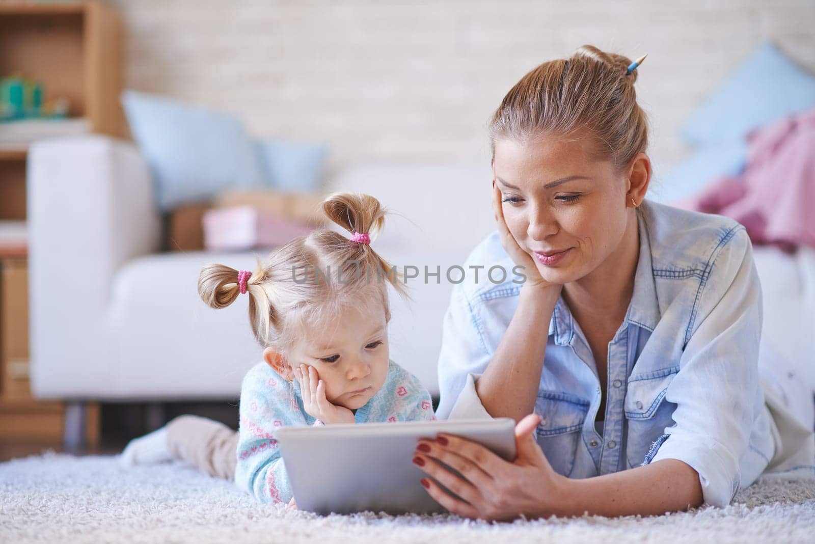 Young mother and daughter with digital tablet lying on the floor and resting online