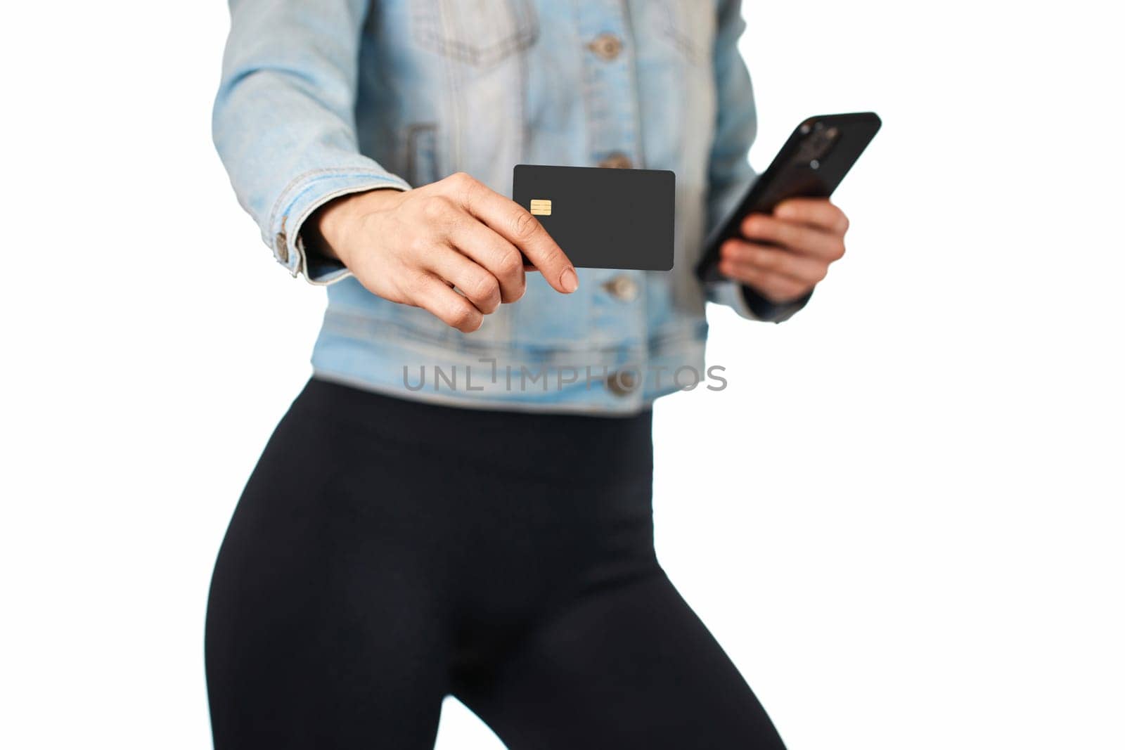 woman in denim holding mobile phone and black premium credit bank card on white background. woman paying with plastic credit card on smartphone app,