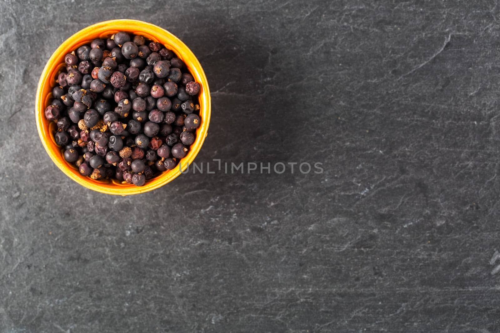 Bowl of juniper berries on stone surface with copy space.