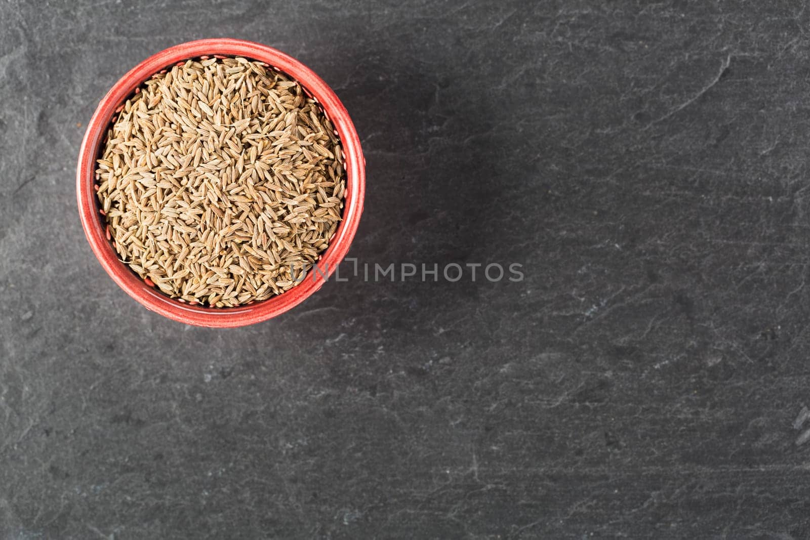 Bowl of caraway seeds on stone surface with copy space.
