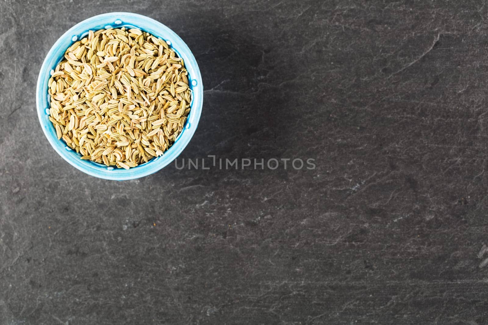 Bowl of fennel seeds on stone surface with copy space.