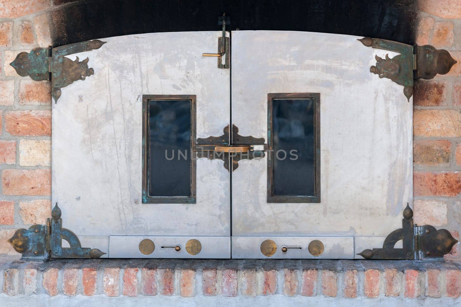 Frontal view on the doors of a bakery oven with brass fittings and windows in a brick wall.